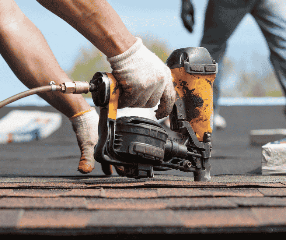 Close-up of a roofing contractor using a pneumatic nail gun to install asphalt shingles during a residential roof replacement project.