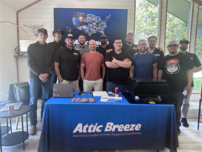 Group of roofing contractors at an Attic Breeze training session with a solar attic fan and literature on a branded table
