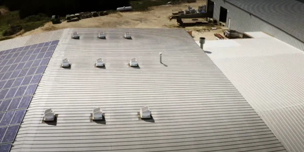Aerial view of a commercial metal roof with rows of solar attic fans and a solar panel array