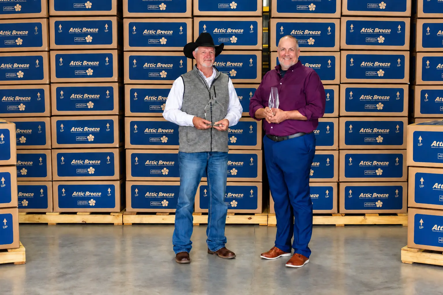 Two Attic Breeze team members holding awards in front of stacked Attic Breeze boxes